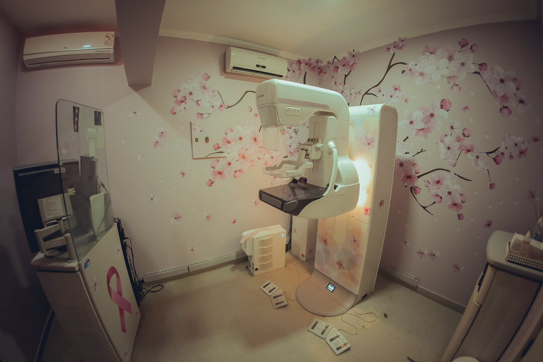 Uma mulher se realizando o exame de mamografia com o acompanhamento de uma profissional med-rad